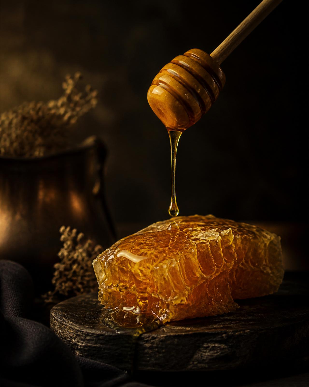 Amber honey drizzling onto raw honeycomb on dark stone